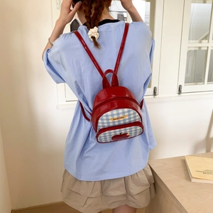 Dettaglio dello zaino in pelle verniciata rossa con patch mela e tessuto a scacchi blu