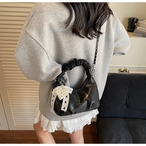 Detail of black pleated handbag with pearl bow charm and chain strap in daily scene
