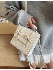 Chic white square crossbody bag with bow accents and adjustable strap shown on model