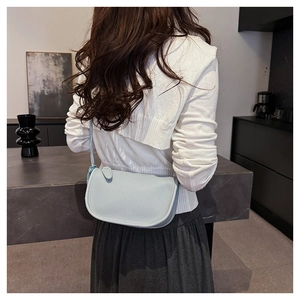 Détail du sac selle en cuir grainé bleu clair porté sur un pull en maille blanc