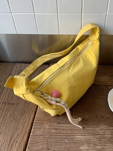 Bright yellow crescent crossbody bag with decorative heart pendant and knot strap design