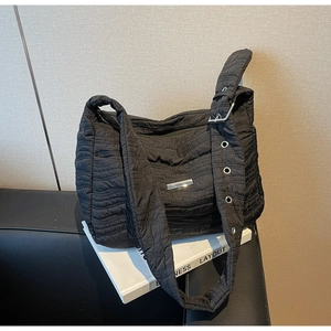 Detail of black quilted shoulder bag featuring wide strap with metal eyelets and logo plate