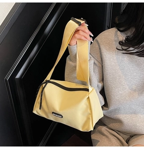 Détail du sac bandoulière beige en toile avec large sangle et logo de la marque