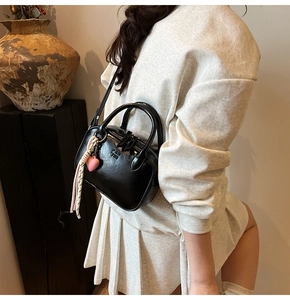 Détail d'un sac bandoulière noir avec breloque cœur rose et double fermeture éclair