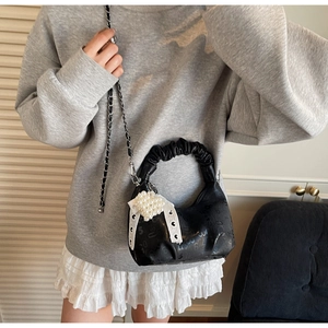 Detail of black pleated handbag featuring pearl heart charm and metallic chain strap
