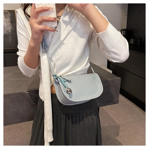 Détail du sac selle bleu clair avec texture litchi et bandoulière à nœud tressé