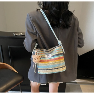 Detail of colorful woven straw bucket bag with cute bear pendant and blue strap