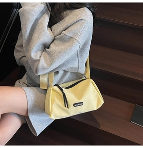 Détail du sac bandoulière jaune clair en toile avec sangle réglable et logo sur escalier