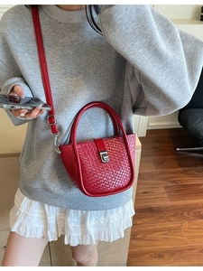 Fashionable red woven bucket bag with top handle and crossbody strap on indoor model