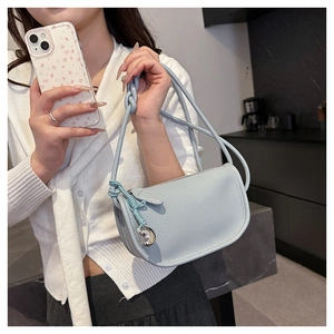 Détail du sac selle en cuir grainé bleu clair avec bandoulière nouée et breloque cœur