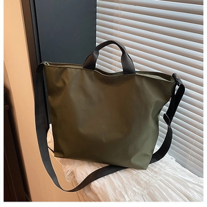 Detail of army green nylon tote bag with black handles on a white fabric background