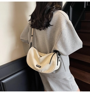 Minimalist cream canvas half-moon crossbody bag with black knotted zipper and logo detail