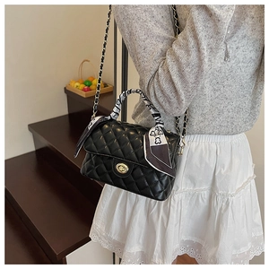Close-up of quilted black crossbody bag with gold twist lock and printed silk scarf