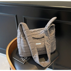 Close-up of grey quilted puff shoulder bag with wide strap and metallic eyelet details