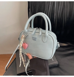 Détail du sac bandoulière bleu clair avec ruban rayé et pendentif cœur rose