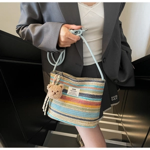 Detail of colorful woven straw bucket bag with blue shoulder strap and bear charm