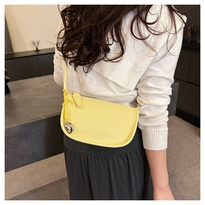 Détail d'un sac besace jaune vif en cuir grainé avec un pendentif en forme de cœur argenté