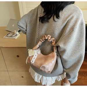 Brown pleated shoulder bag with embossed texture and pearl bow charm shown in lifestyle