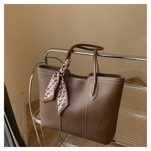 Close-up of dark brown lychee leather tote with white contrast stitching and silk scarf detail