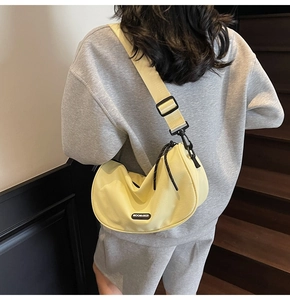 Close-up of pale yellow crescent nylon bag with adjustable black strap and woven zipper puller