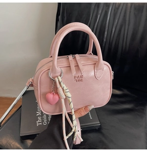 Gros plan détaillé d'un sac à main rose en cuir avec pendentif cœur et sangle tissée