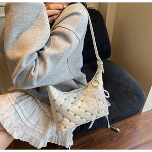 Détail d'un sac à main matelassé blanc avec clous argentés et breloque en perles