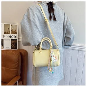 Detail of yellow lychee grain Boston bag featuring a colorful woven tassel charm
