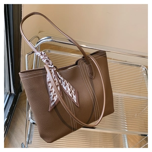Detail of brown lychee grain leather tote bag with white stitching and decorative silk scarf