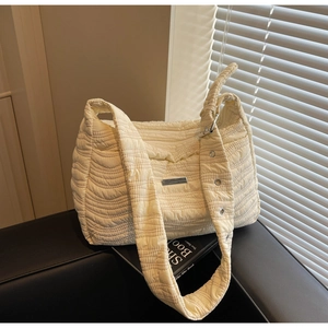 Close-up of beige wave-quilted tote bag with wide strap and metal accents on a table