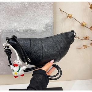 Detail of black croissant bag with litchi leather texture and a cute duck charm