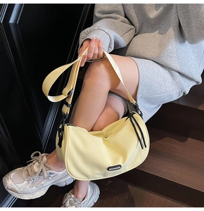 Detail of light yellow crescent pillow bag with black adjustable strap and brand label