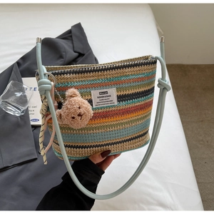 Detail of colorful striped woven bucket bag with blue leather handle and plush bear charm