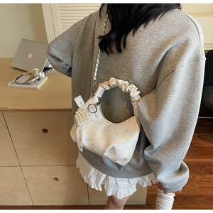 Detail of white half-moon bag with embossed texture, lace bow and pearl heart charm