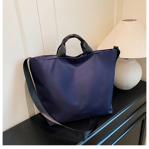 Detail of navy blue nylon tote bag with black straps in a minimalist home setting