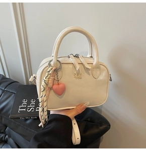 Détail du sac en cuir crème avec double fermeture éclair, breloque cœur et nœud rayé