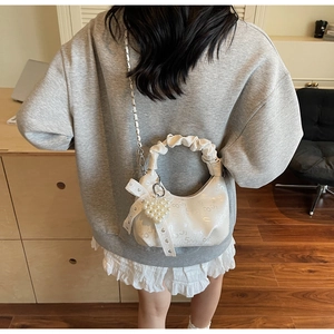 Detail of white pleated handbag with silver chain, heart pendant and lace bow accessory