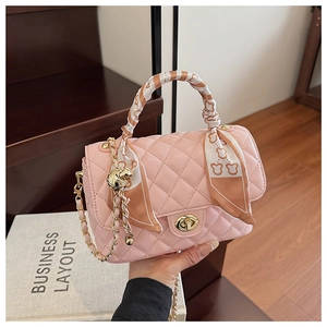 Detail of pink quilted box bag with decorative scarf-wrapped handle and gold chain strap