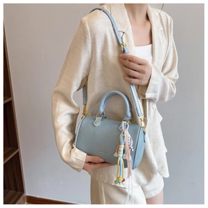 Detail of light blue cylinder bag with litchi texture, metal handle and rainbow tassel