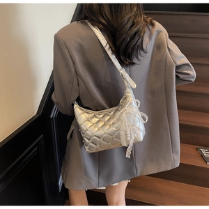Silver quilted crossbody bag with pearl bow pendant worn over a grey blazer on stairs