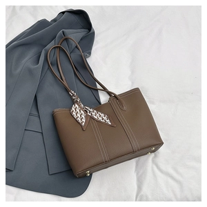 Detail of dark brown tote bag featuring white contrast stitching and gold metal feet