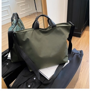 Detail view of olive green nylon tote bag with black wide straps on a mirrored surface