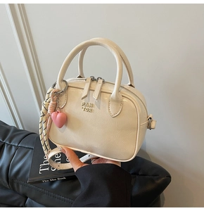 Détail du sac Boston en similicuir beige avec logo en métal et breloque cœur