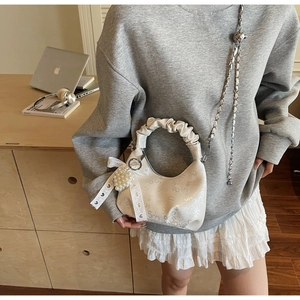 Detail of white half-moon bag featuring pleated handle, pearl heart charm and digital print