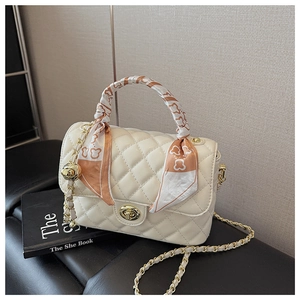 Close-up of cream quilted box bag with golden twist lock and decorative orange silk scarf