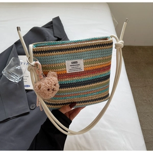 Detail shot of a colorful striped straw bucket bag featuring a cute brown plush bear charm