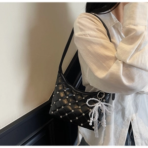 Détail d'un sac bandoulière matelassé noir avec strass et breloque noeud en perles