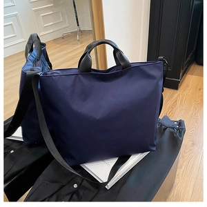 Detail of navy blue nylon tote bag with black leather handles and shoulder strap