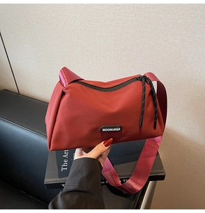 Gros plan sur un sac bandoulière en nylon bordeaux avec large sangle et logo de marque