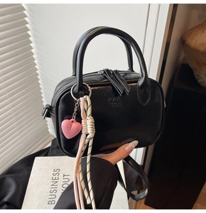 Détail d'un sac à bandoulière en cuir verni noir avec double zip et charme de coeur