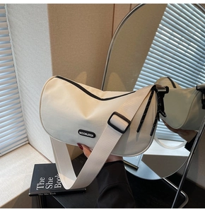 Detail of a cream crescent shoulder bag with a wide strap and a black brand logo